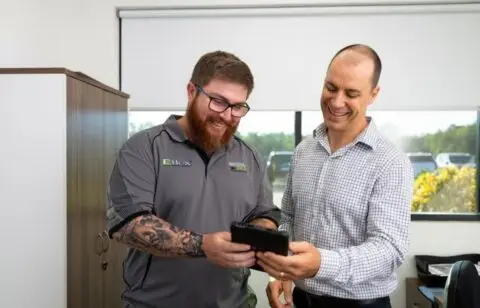Two men smiling at tablet in office
